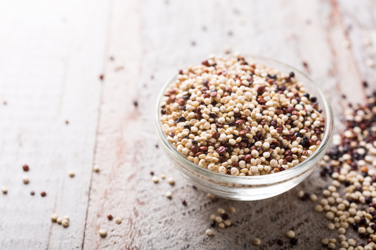 Mixed raw quinoa in glass bowl on white rustic wooden background