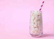Glass full of sugar cubes on a pink background