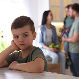 Unhappy little boy feeling jealous while parents spending time with his sister at home