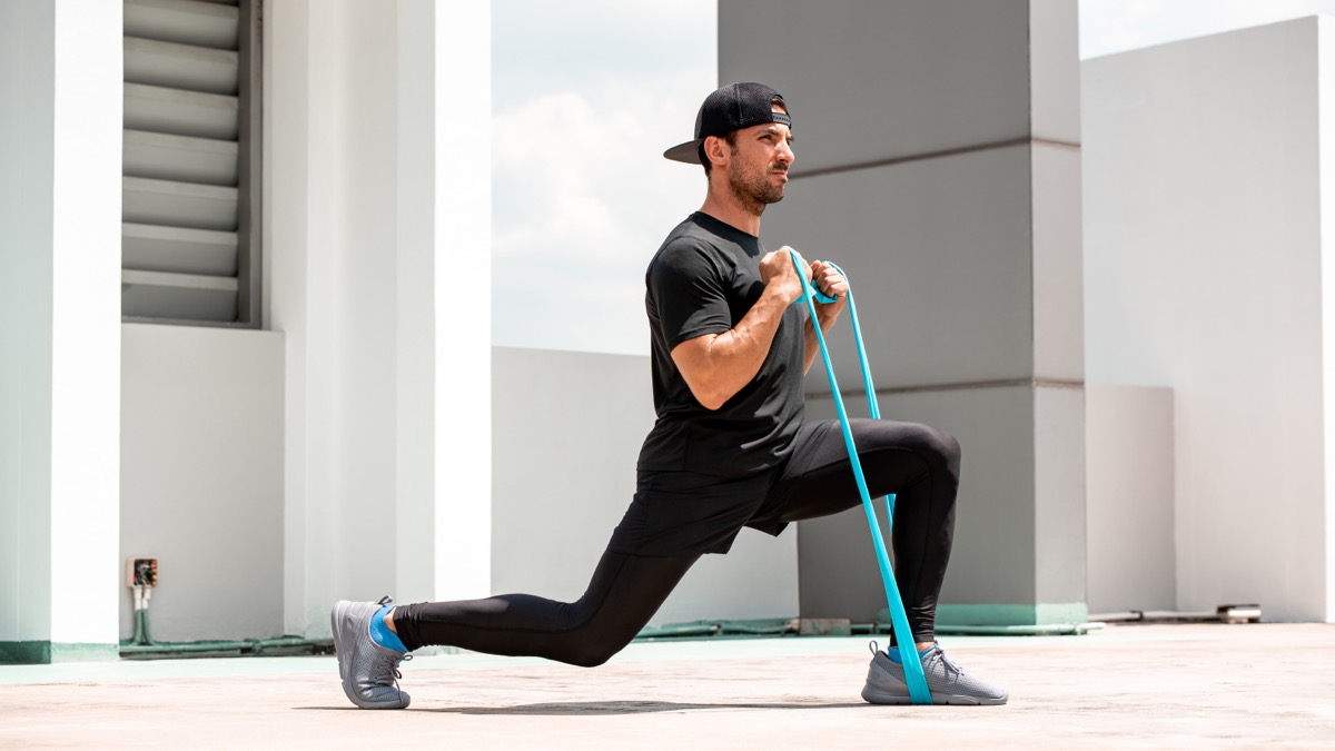 Man doing lunge workout with resistance band outdoors in the sun