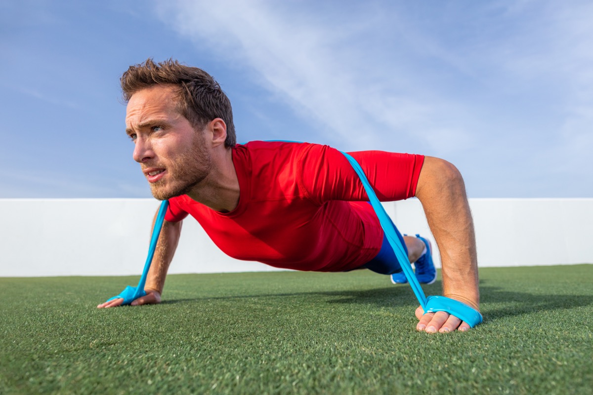 Man doing push ups using resistance bands on outdoor turf