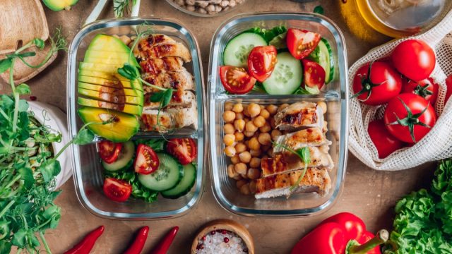 Healthy meal prep containers with chickpeas, chicken, tomatoes, cucumbers and avocados.