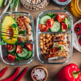 Healthy meal prep containers with chickpeas, chicken, tomatoes, cucumbers and avocados.