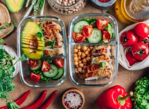 Healthy meal prep containers with chickpeas, chicken, tomatoes, cucumbers and avocados.