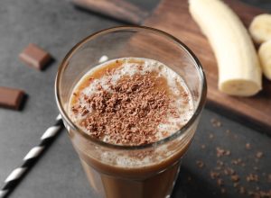 Glass with chocolate protein shake on table, with banana in the background
