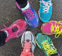 Overhead view of 6 brighlty colored runners' shoes on wet pavement