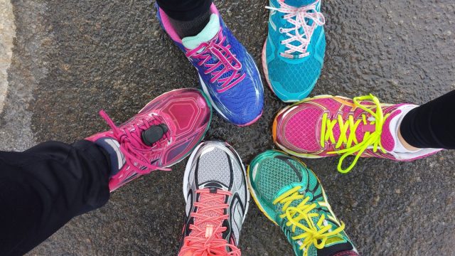 Overhead view of 6 brighlty colored runners' shoes on wet pavement