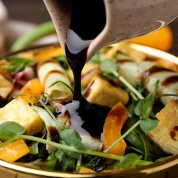 Pouring balsamic vinegar onto delicious salad with tofu and vegetables in bowl, closeup