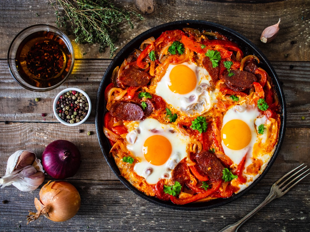 Shakshuka dish with fried eggs with chorizo and vegetables in frying pan