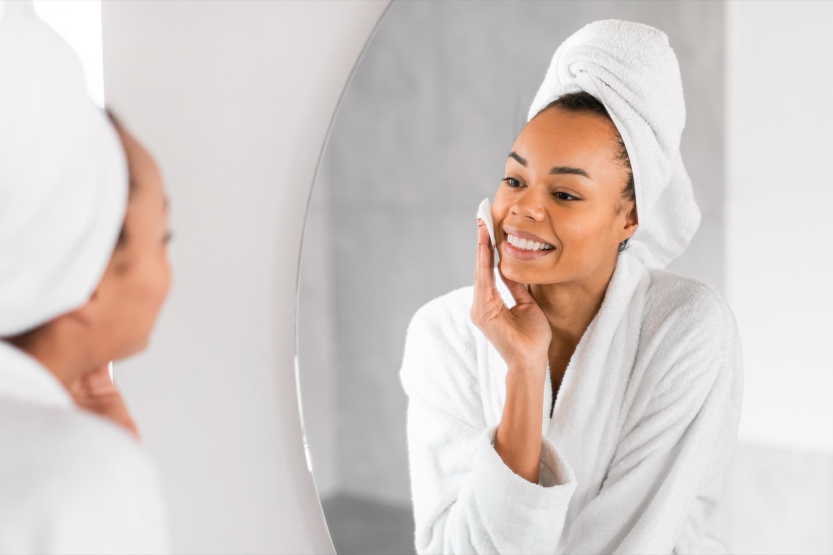 Smiling woman in a white robe uses micellar water on her cheek