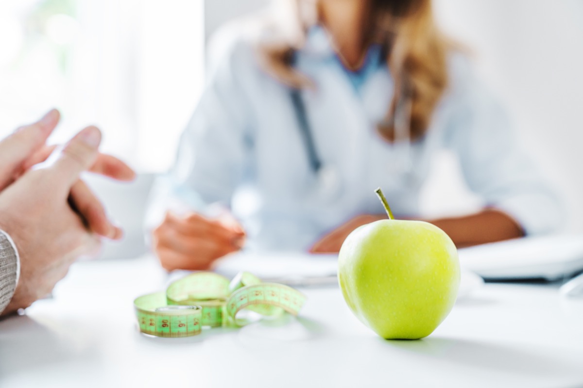 closeup blurred image of weight-loss doctor talking to a patient with an apple on the table