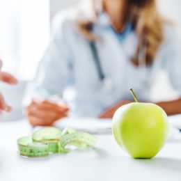 closeup blurred image of weight-loss doctor talking to a patient with an apple on the table