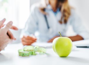 closeup blurred image of weight-loss doctor talking to a patient with an apple on the table