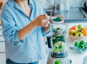 Woman adding spirulina green powder to green smoothie