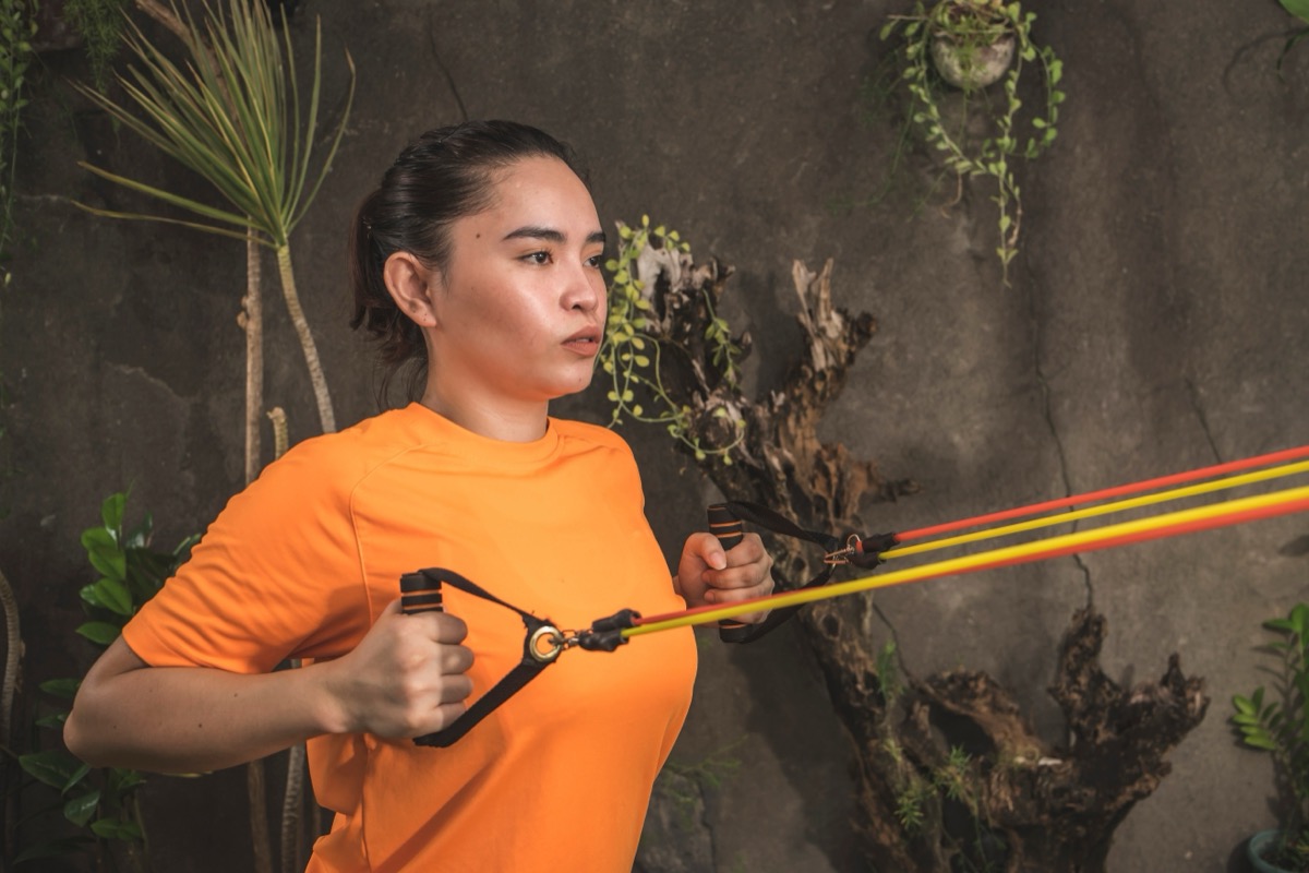 Young woman wearing an orange t-shirt doing standing rows with resistance bands