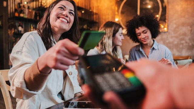 Happy young woman paying bill with a contactless credit card in a restaurant