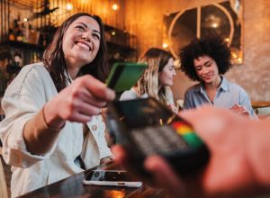 Happy young woman paying bill with a contactless credit card in a restaurant