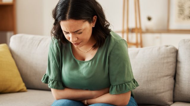 Woman sitting on a sofa holding her abdomen in pain
