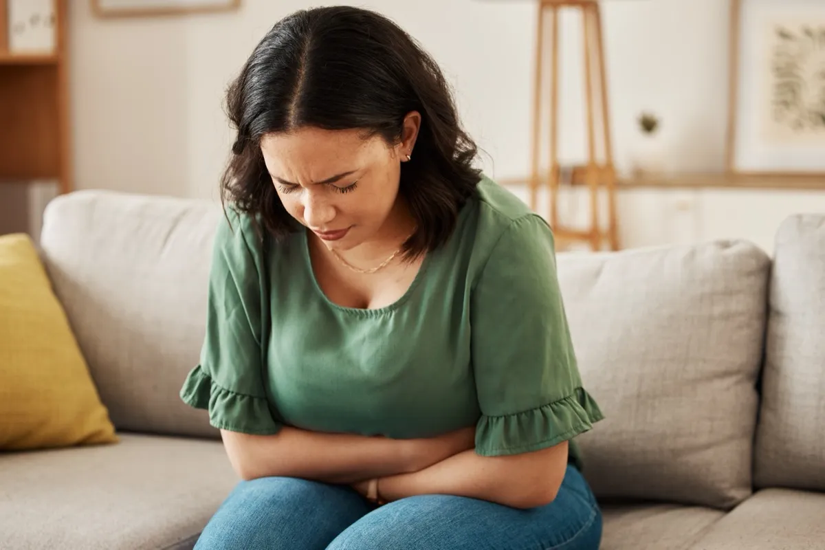 Woman sitting on a sofa holding her abdomen in pain