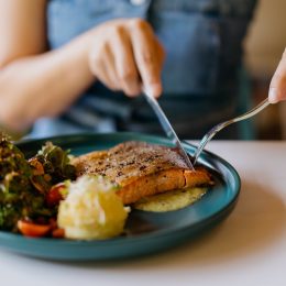 Close up shot of woman eating pan fried salmon with table knife and fork in cafe