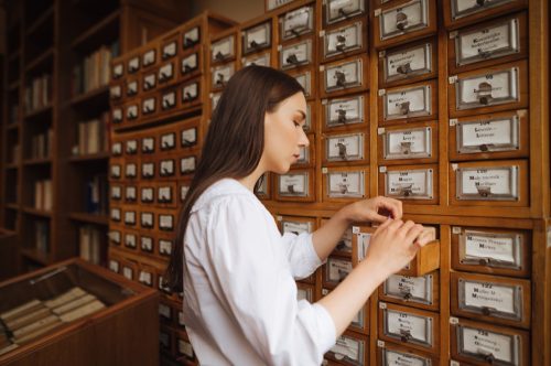 woman in a white blouse searches for information in the archives of the public library, opens a drawer.