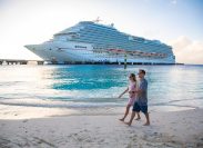 Middle aged couple enjoying a Caribbean Cruise vacation together. Candid photo of a couple holding hands and walking together on a beach with a Cruise ship in the background