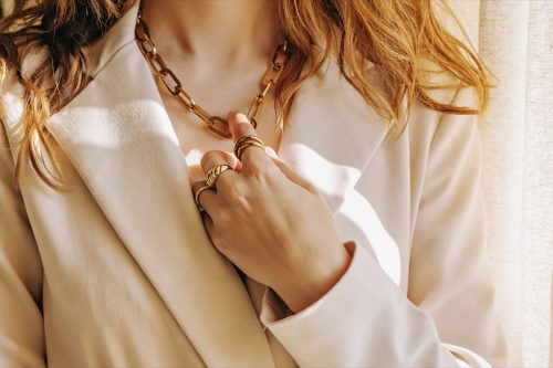 Close-up of female hand with rings touching her golden chain necklace, natural morning light