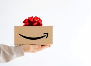 A hand holding out an Amazon box with a gift bow on top of it