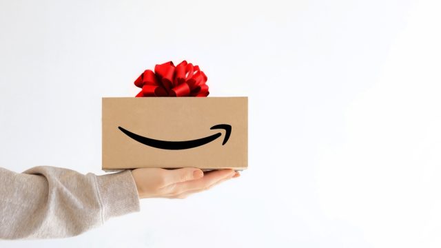 A hand holding out an Amazon box with a gift bow on top of it