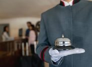 A close up of a bellhop's hand holding a bell in a hotel lobby