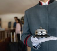 A close up of a bellhop's hand holding a bell in a hotel lobby