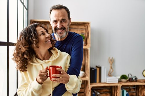 Middle age couple smiling happy and drinking coffee. Leaning on the window at home.