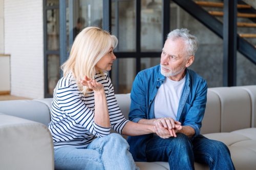Elderly man listening carefully and try to understand woman. Sitting on sofa at home. Reliable partner. Supportive spouse. Loving, caring husband support wife