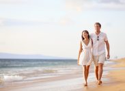 couple wearing white clothes walking arm-in-arm on the beach