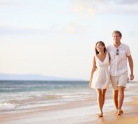 couple wearing white clothes walking arm-in-arm on the beach