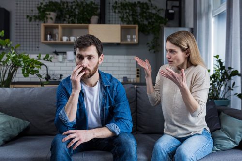 Family quarrel, man and woman sitting on sofa at home. angry woman yells at her husband, blames. The man is silent. He listens, holds his head, embarrassed