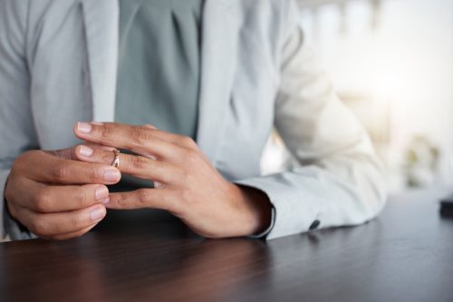 Hand or finger, ring and divorce of a woman at table with doubt, anxiety or thinking about depression. Female person taking off wedding band jewellery for separation counselling, cheating or mistake