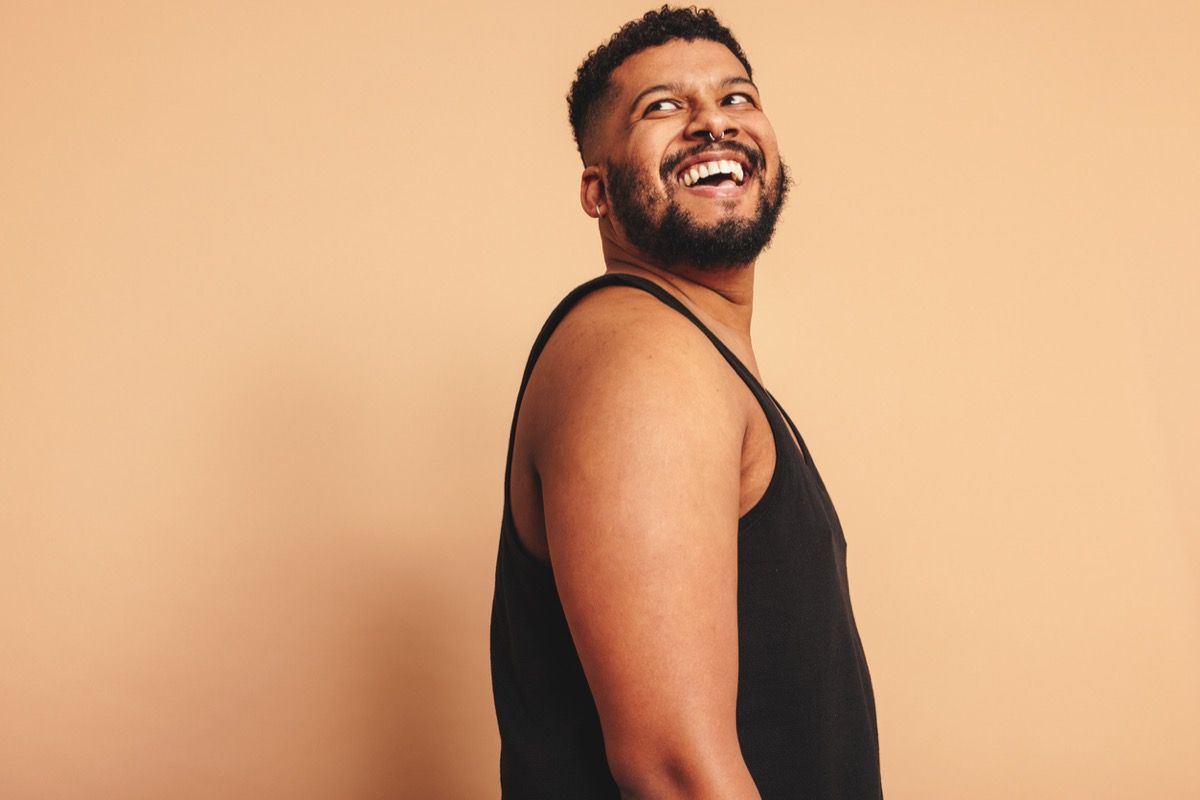 Bearded man looking away with a smile on his face in a studio. Happy young man standing alone against a studio background. Body positive man feeling comfortable in his natural body.