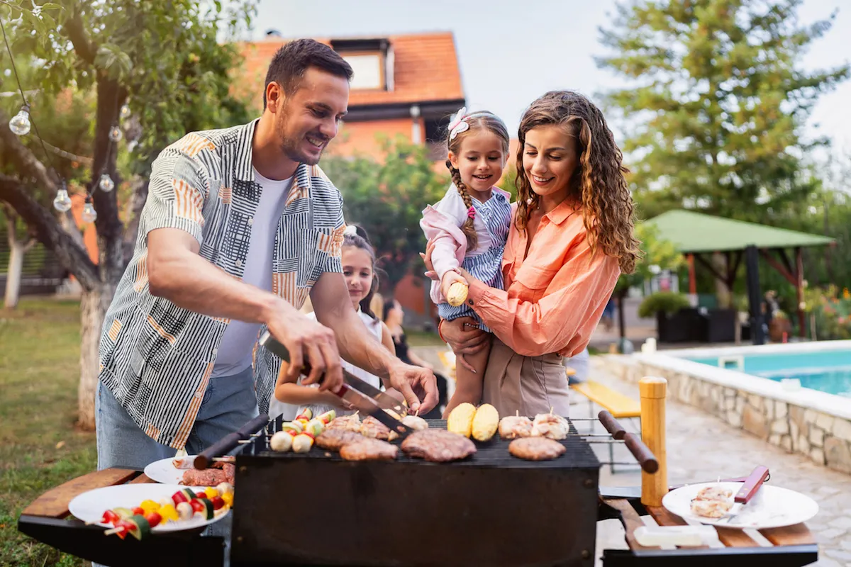 Young couple, wife and husband with daughters making barbecue for rest of their family, during family reunion