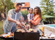 Young couple, wife and husband with daughters making barbecue for rest of their family, during family reunion