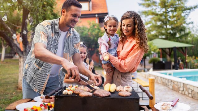 Young couple, wife and husband with daughters making barbecue for rest of their family, during family reunion