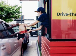 Hand Man in car receiving coffee in drive thru fast food restaurant. Staff serving takeaway order for driver in delivery window. Drive through and takeaway for buy fast food for protect covid19.