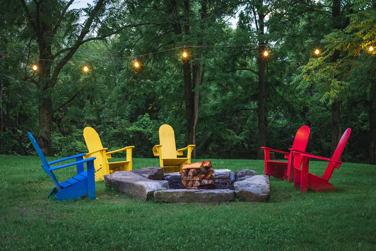 A fire pit and adirondack chairs sit under string lights, ready to enjoyed