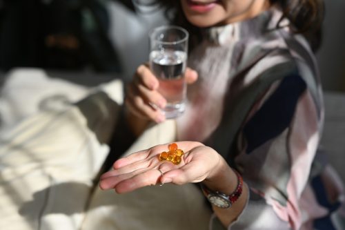 Wellness, Vitamins and Supplements concept, Grey haired senior woman with omega 3 supplement capsule in her hand.