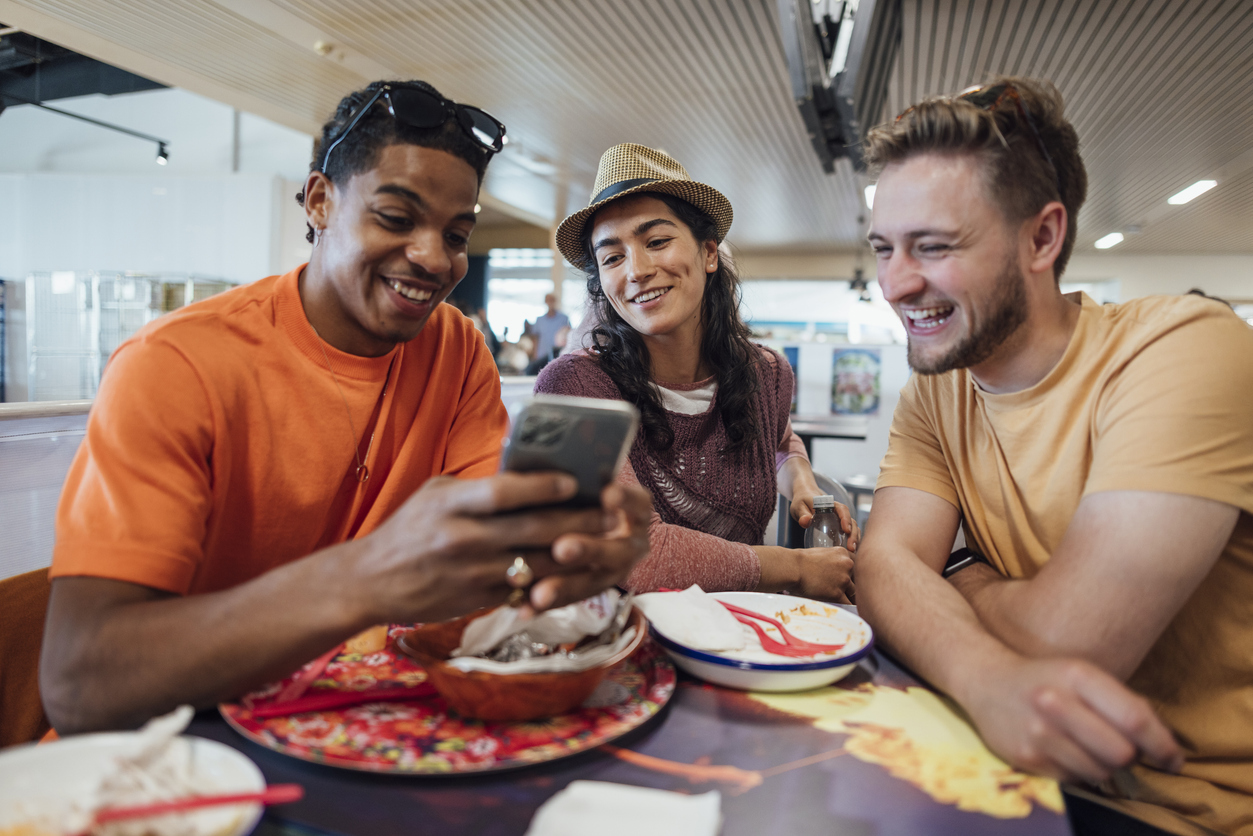 A group of friends looking at a phone while eating at a restaurant in an airport