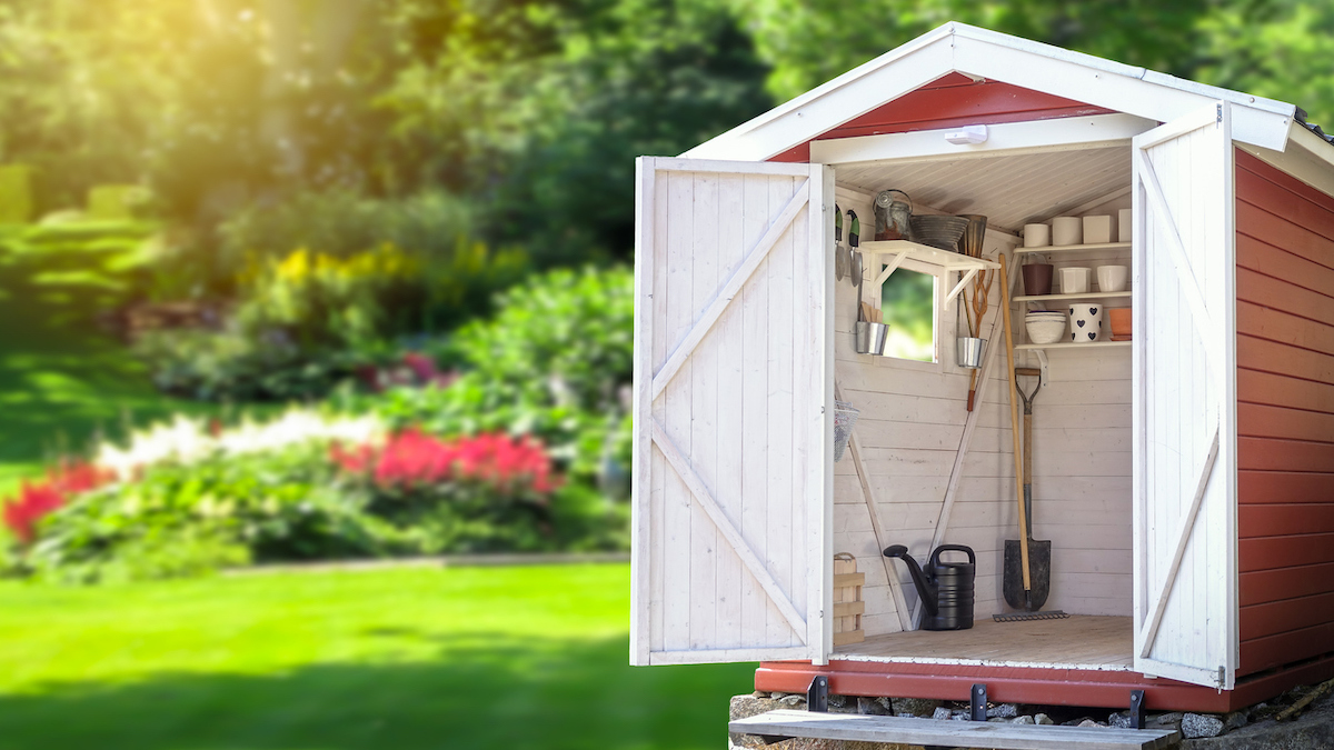 Storage shed filled with gardening tools with a lush garden in the background