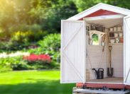 Storage shed filled with gardening tools with a lush garden in the background