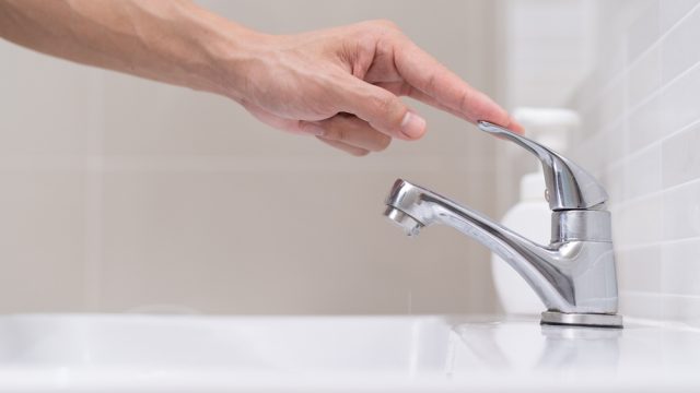 A hand turning off a faucet on a bathroom sink