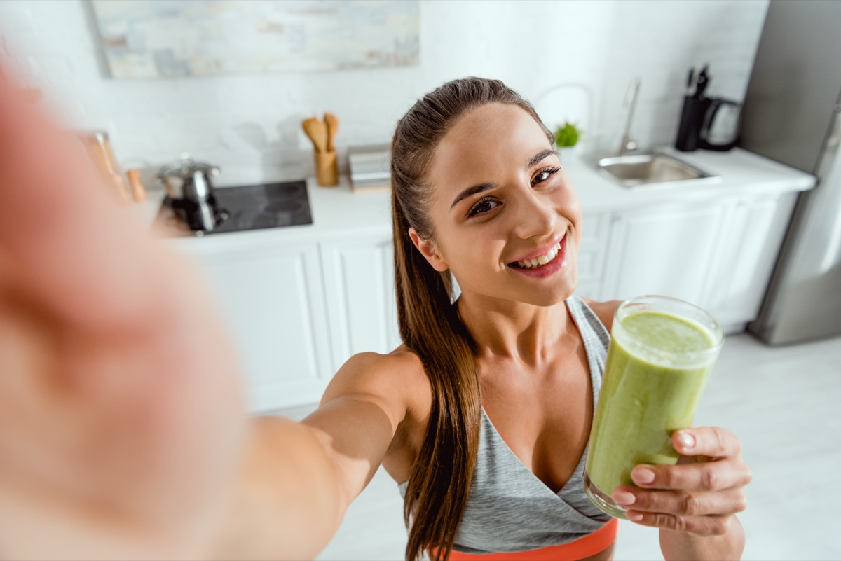 selective focus of positive girl holding green smoothie and looking at camera