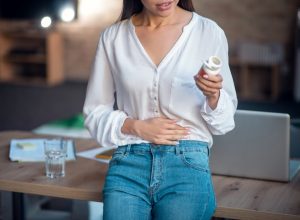 Feeling pain. Pleasant young woman putting hand on her stomach while feeling pain in it